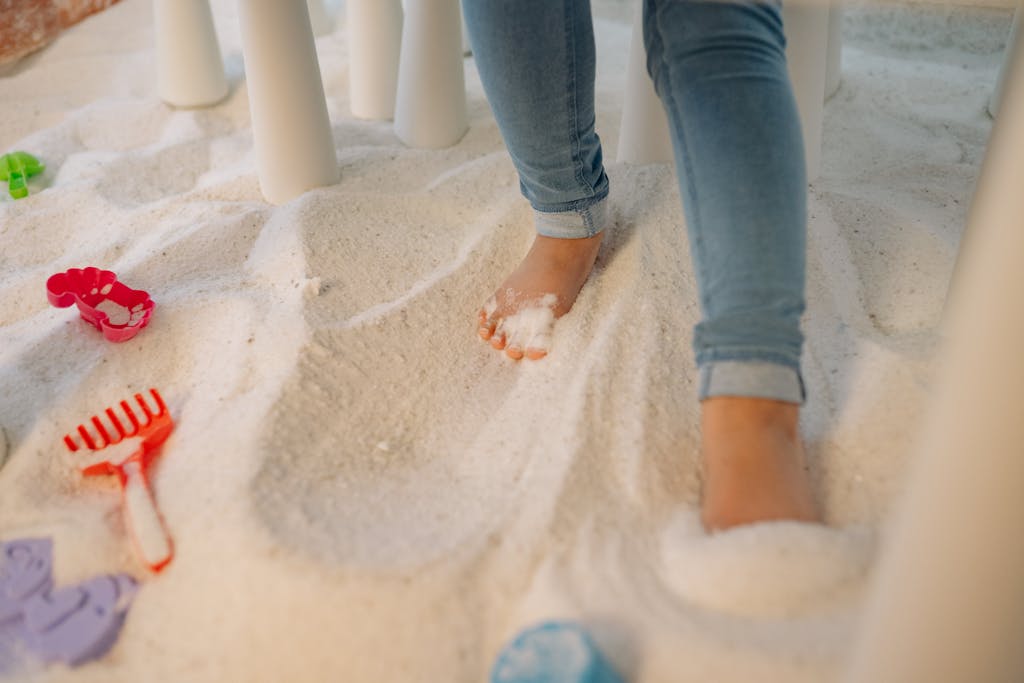 A child enjoying an indoor sand play area, standing barefoot among colorful toys.