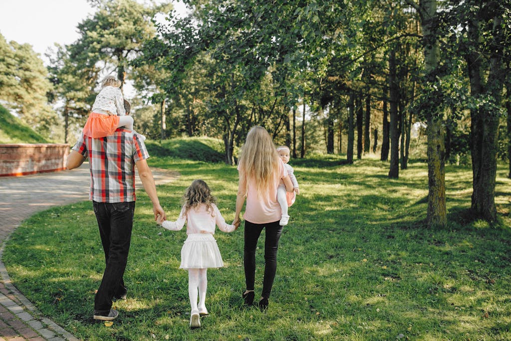 A family enjoying a walk under dappled sunlight in a lush green park.