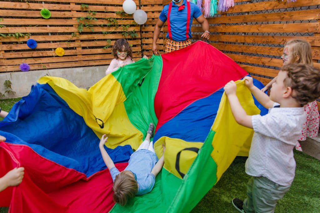 A group of children joyfully playing with a colorful parachute in a backyard setting.