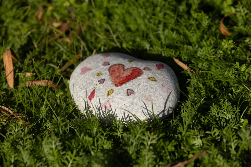 A heart-decorated stone lies on vibrant green grass, evoking feelings of love and nature.
