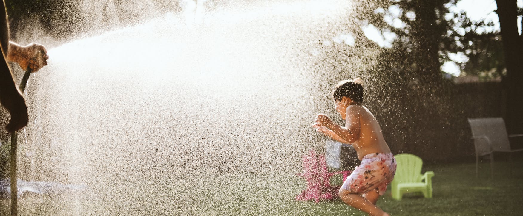 Boy enjoying water spray in backyard on a sunny summer day, capturing fun and joy.