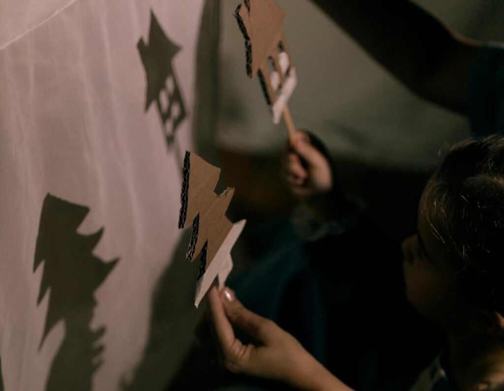 Kids crafting shadow puppets, projected on a white screen, evoking creativity.