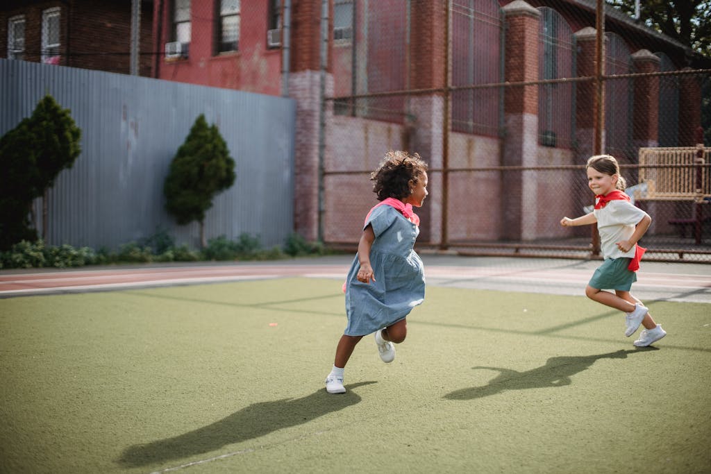 Two children playfully running with capes in an urban playground, enjoying superhero role-play.