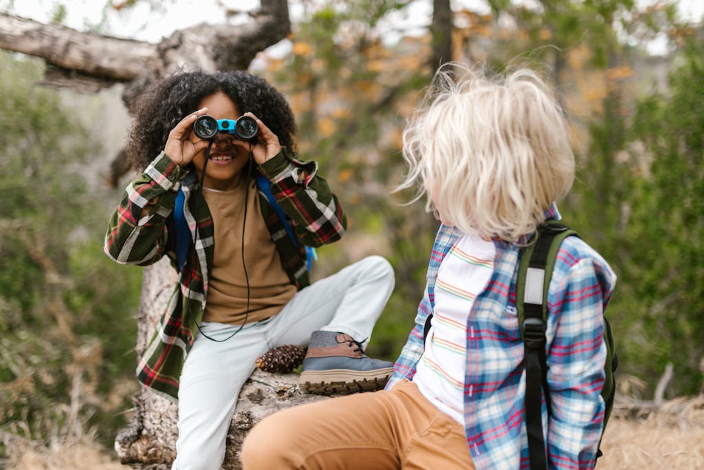 Two children with different hairstyles enjoy a playful day outdoors, exploring with binoculars.